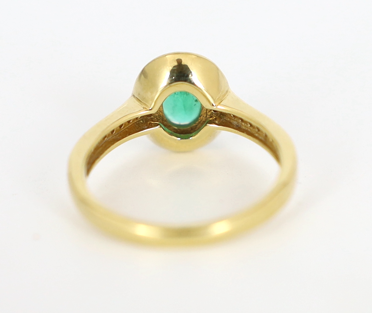 A modern 18ct gold, emerald and diamond set oval cluster ring, with diamond chip set shoulders